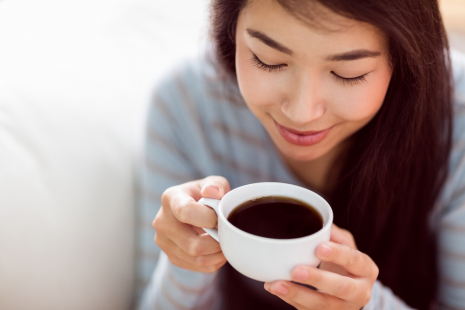Naisen kädessä valkoinen kahvikuppi täynnä kahvia