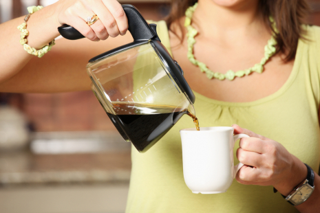 Nainen kaataa kahvia lasisesta kahvikannusta valkoiseen kuppiin